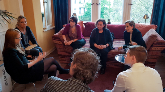 7 Personen sitzen gemütlich auf einer Couch im Wohnzimmer und unterhalten sich