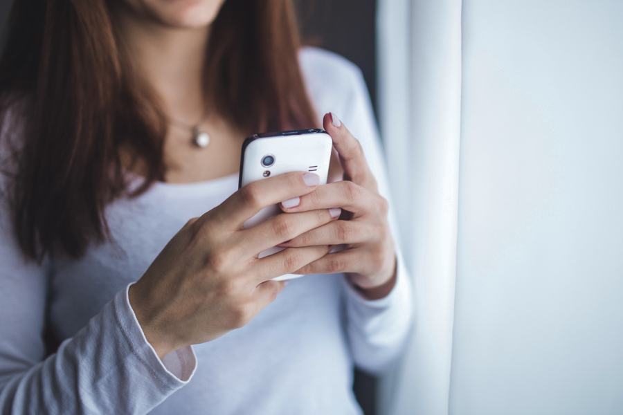 junge Frau mit Handy in der Hand steht am Fenster