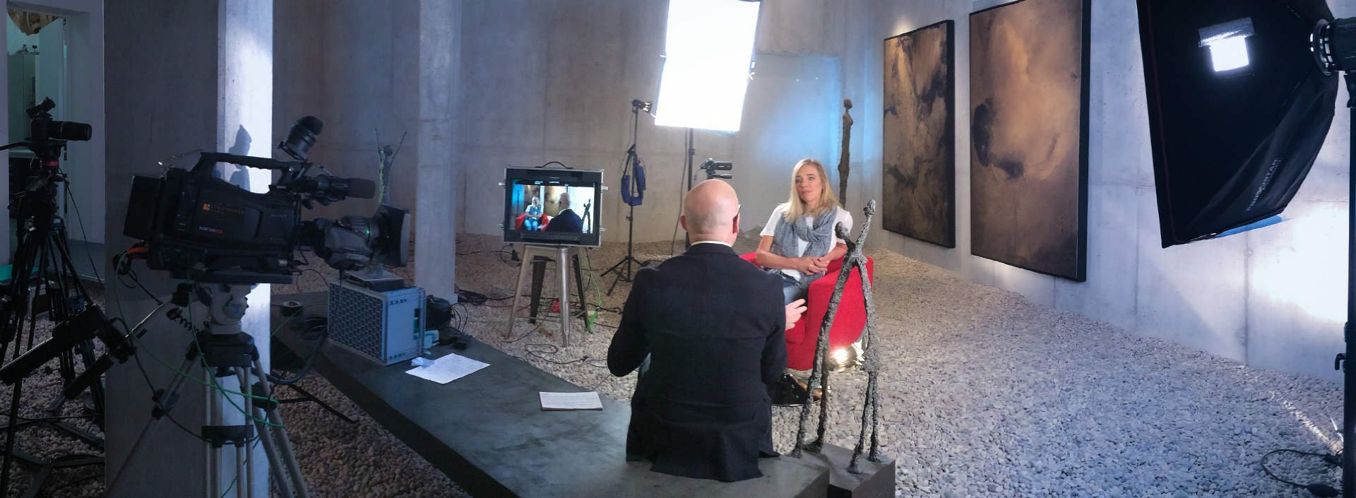 Heidi Sand im Roten Sessel beim Interview mit Filmkameras und Licht in einer Galerie