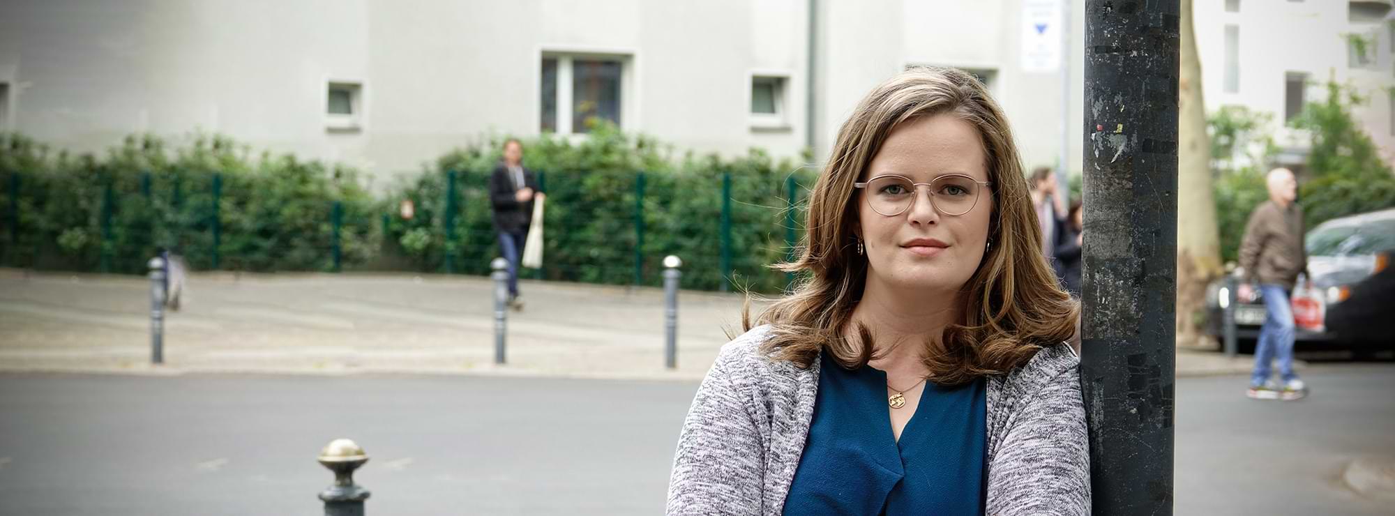 Amelie Fischer lehnt an einer Straßenlaterne und blickt verträumt in die Kamera
