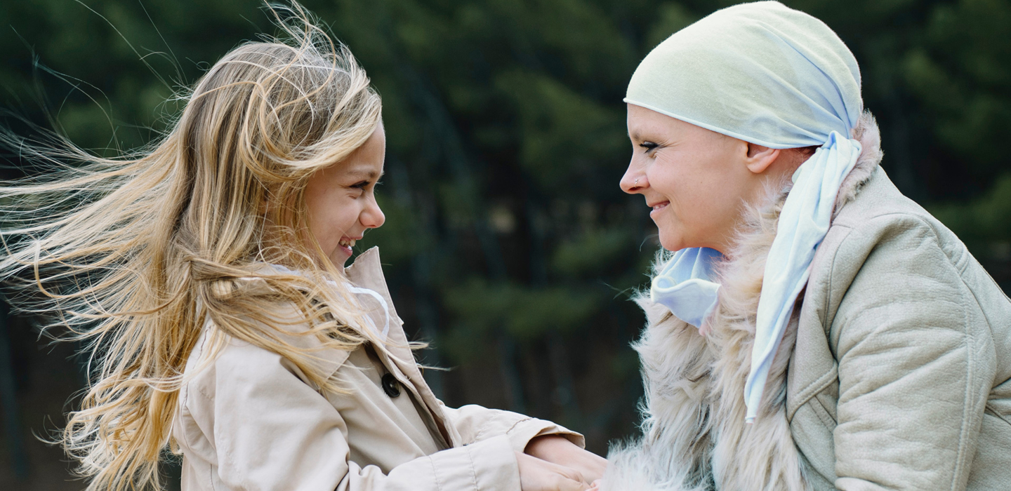 Mitter mit Kopftuch nach Chemotherapie hält die Hände ihres Kindes und beide lachen