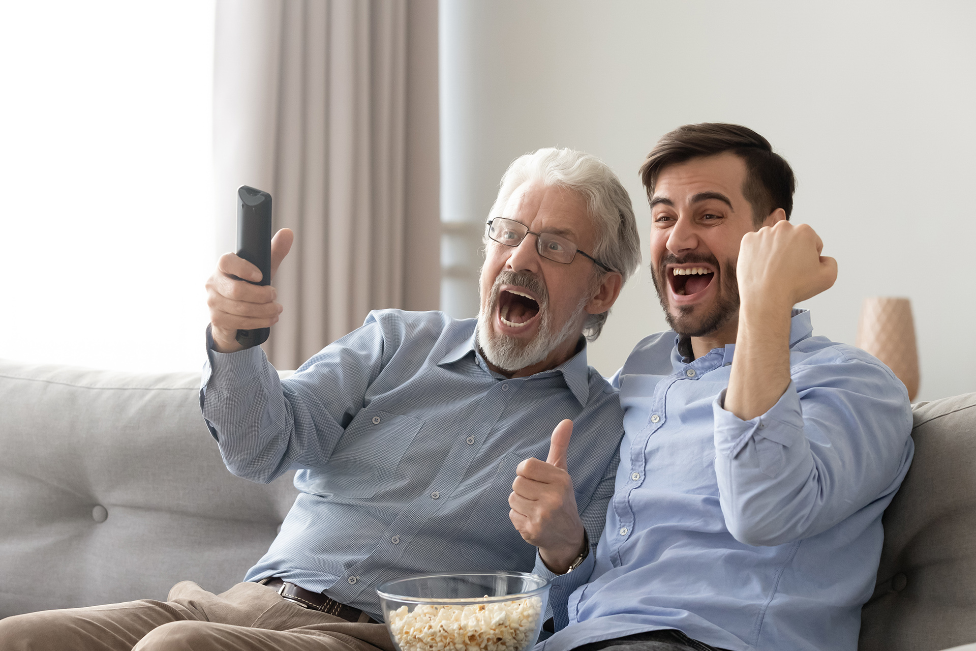 2 Männer unterschiedlichen Alters auf Couch schauen TV und jubeln