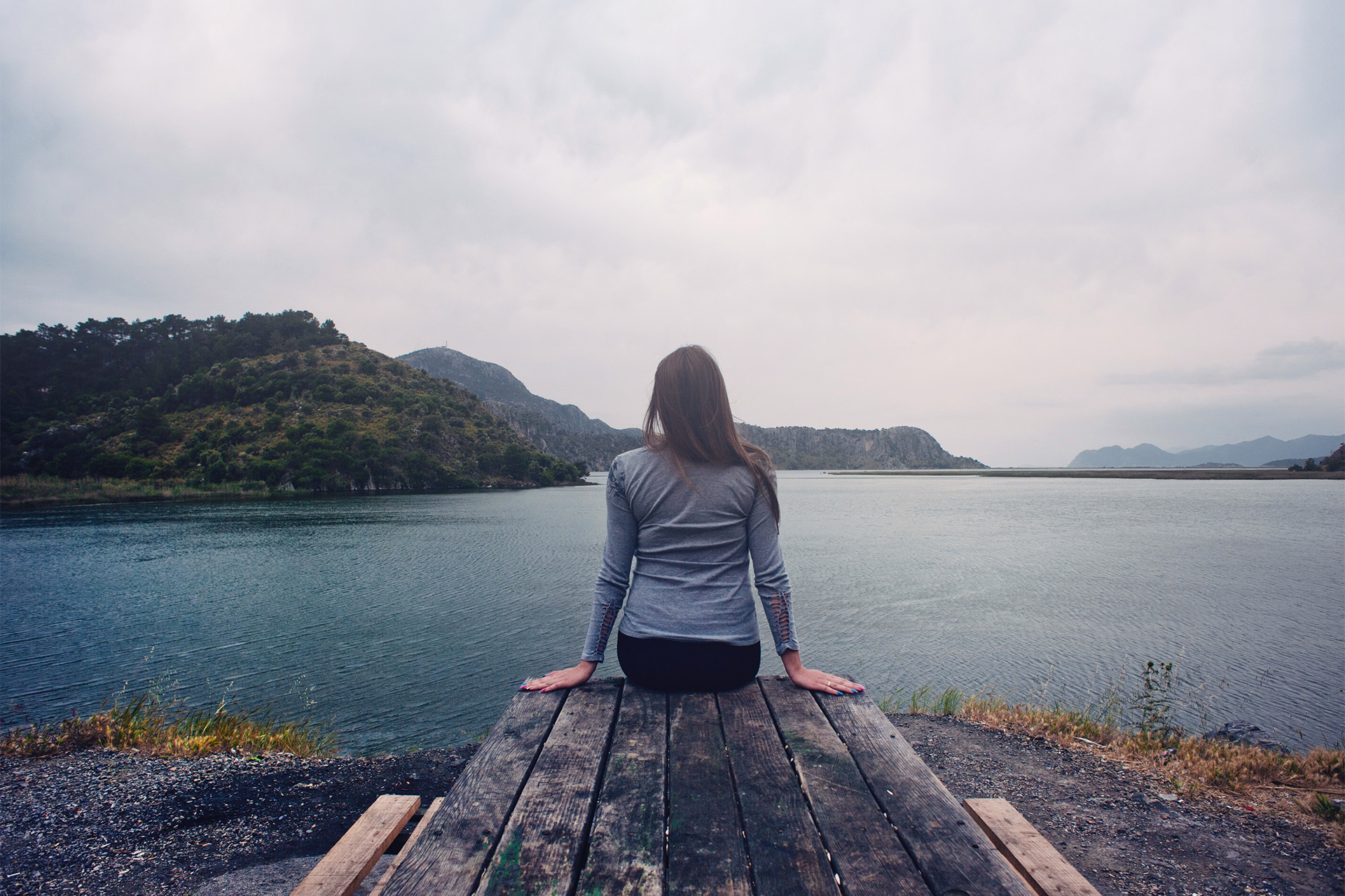 Frau sitzt auf einem Steg an einem See