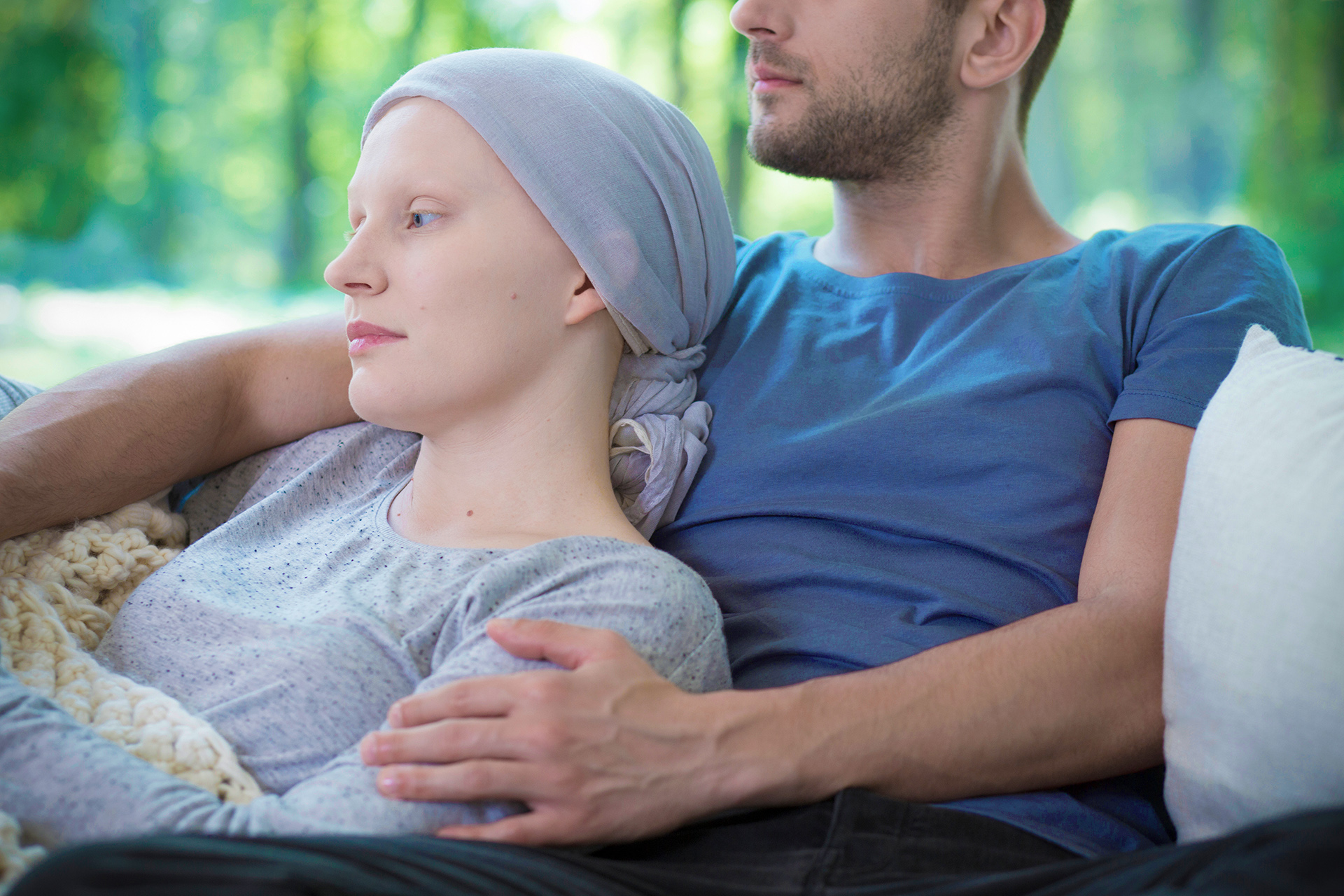 Frau mit Kopftuch während der Chemotherapie liegt zu Hause in den Armen ihres Mannes