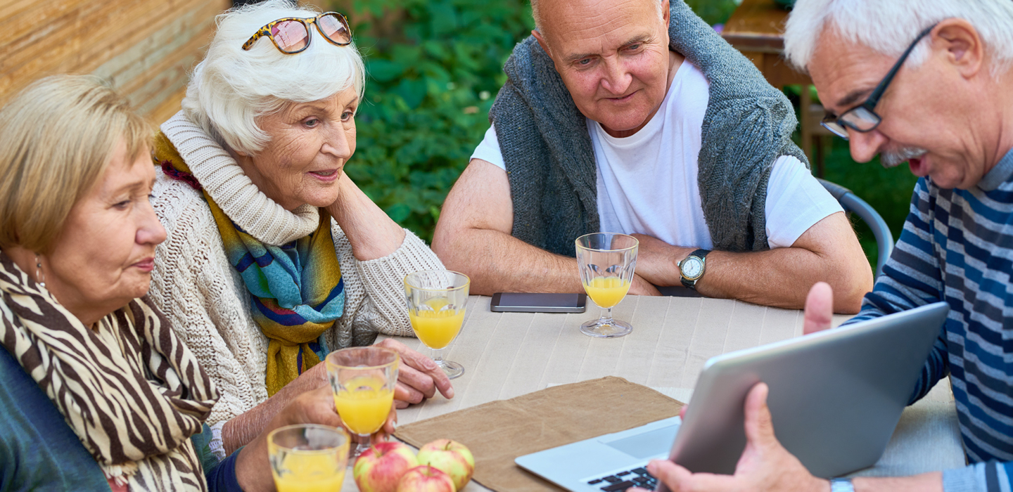 Gruppe von Senioren sitzt am Tisch mit Saft und Obst und schaut auf einen Laptop