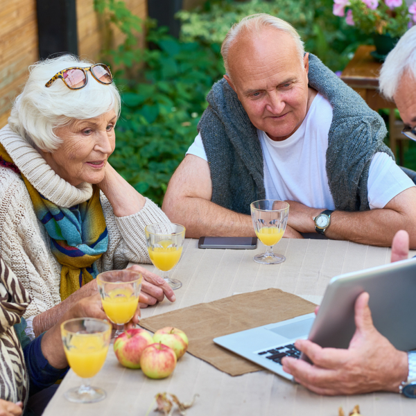 Gruppe von Senioren sitzt am Tisch mit Saft und Obst und schaut auf einen Laptop