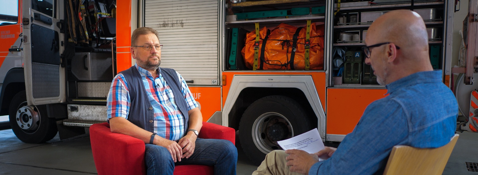 Peter Klaus Rambow sitzt vor einem Feuerwehrauto im Roten Sessel für ein Interview