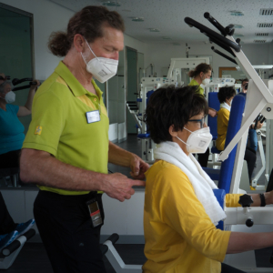 Reha-Patientin trainiert zusammen mit einem Behandler an einem Trainingsgerät die Arme und den Rücken