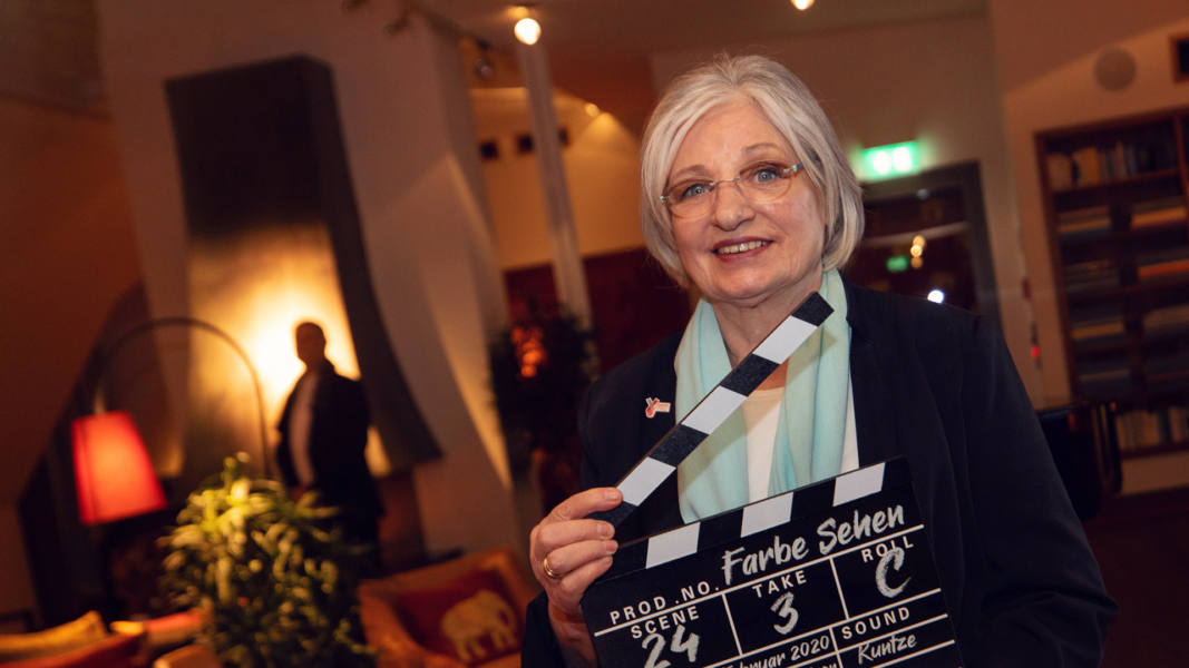 Anita Waldman mit einer Filmklappe in der Hand bei der Premierenveranstaltung "Farbe Sehen"