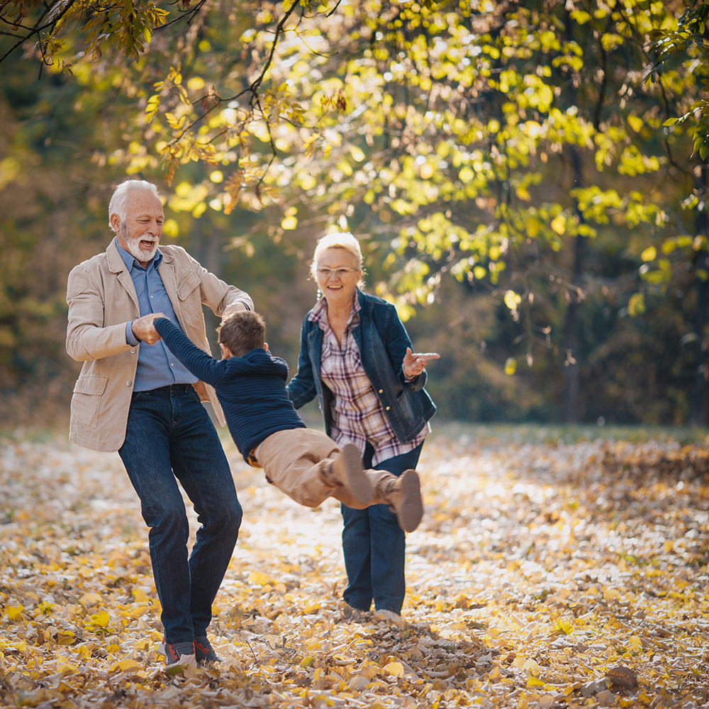 Oma und Opa mit dem Enkel beim Herbstspaziergang, Opa lässt das Kind an den Händen gehalten fliegen