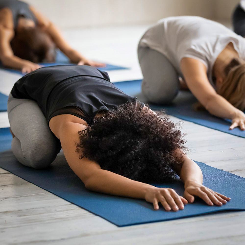 Frauen machen auf Yogamatten Bodenübungen und sind nach vorne gebeugt
